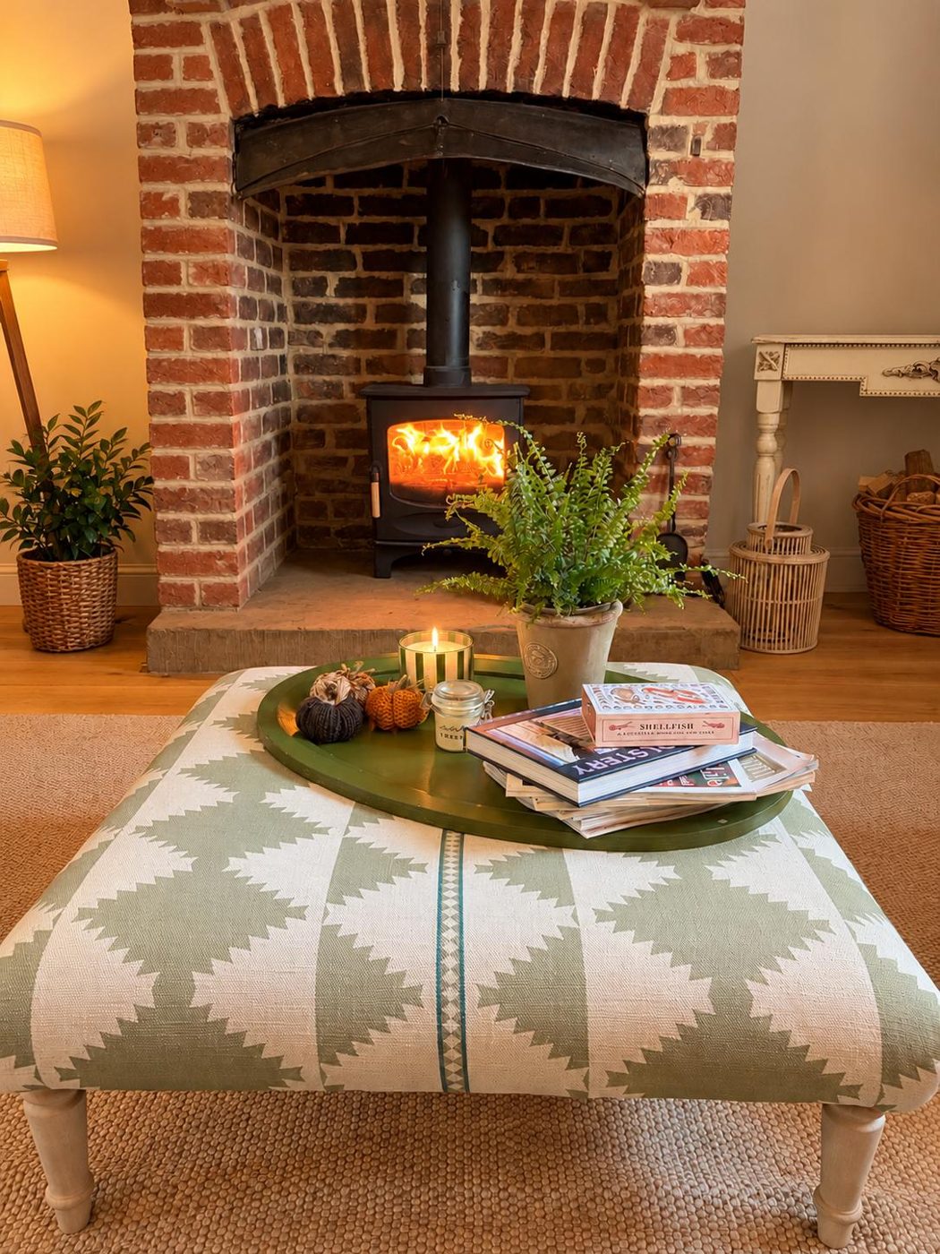 A log burner glowing in a brick fireplace with a green patterned ottoman in front